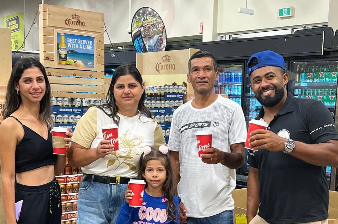 Cinco pessoas, entre elas uma criança, sorrindo e segurando copos vermelhos em uma loja