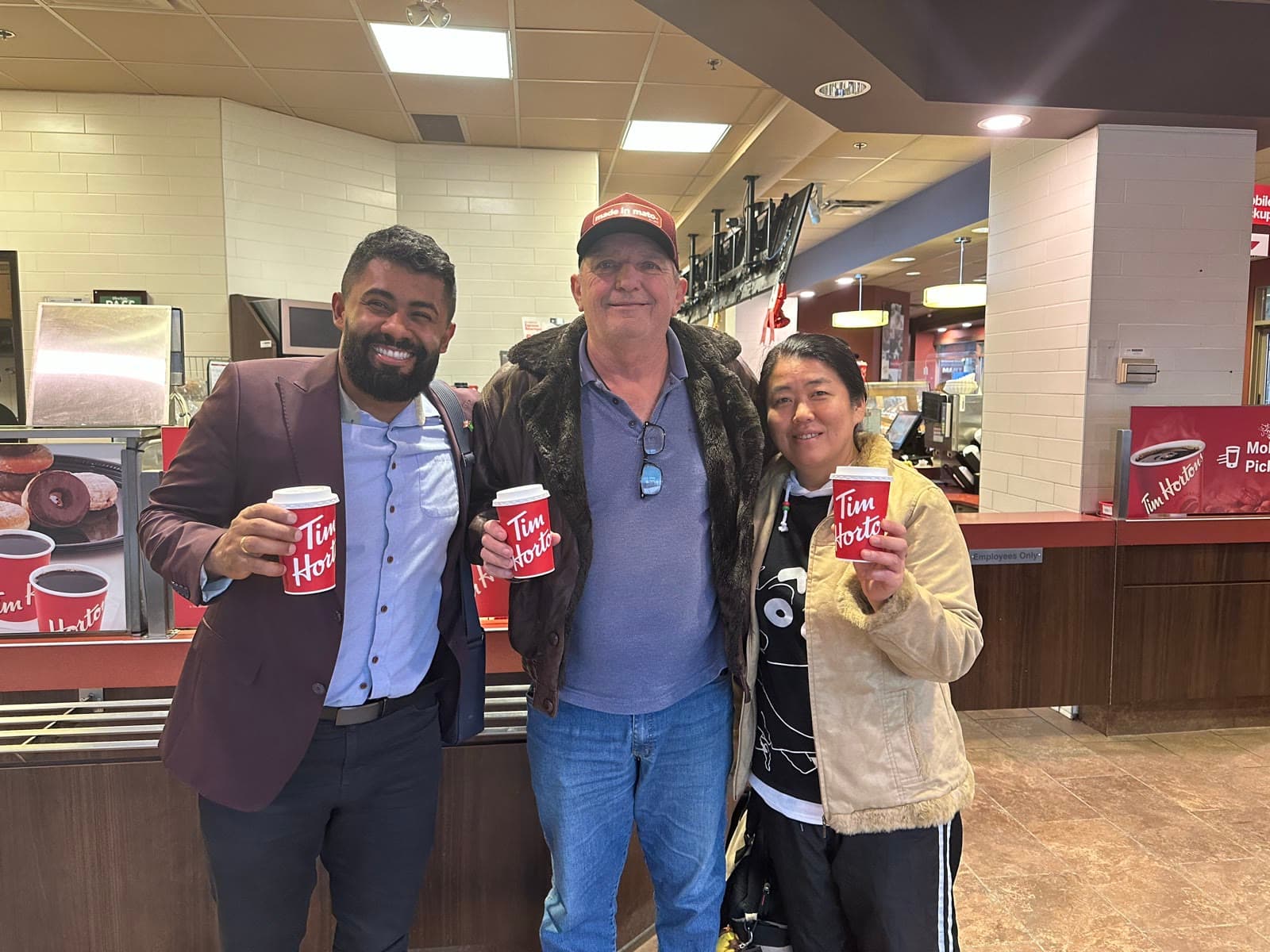 Três pessoas sorrindo e segurando copos em uma lanchonete Tim Hortons